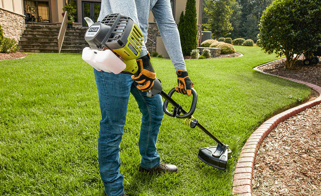 String trimmer edging a lawn along a brick-bordered garden bed